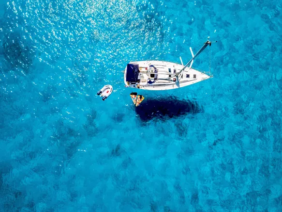 Turquoise and blue ocean with small green islands surrounded by white coasts and a speed boat sailing in the water